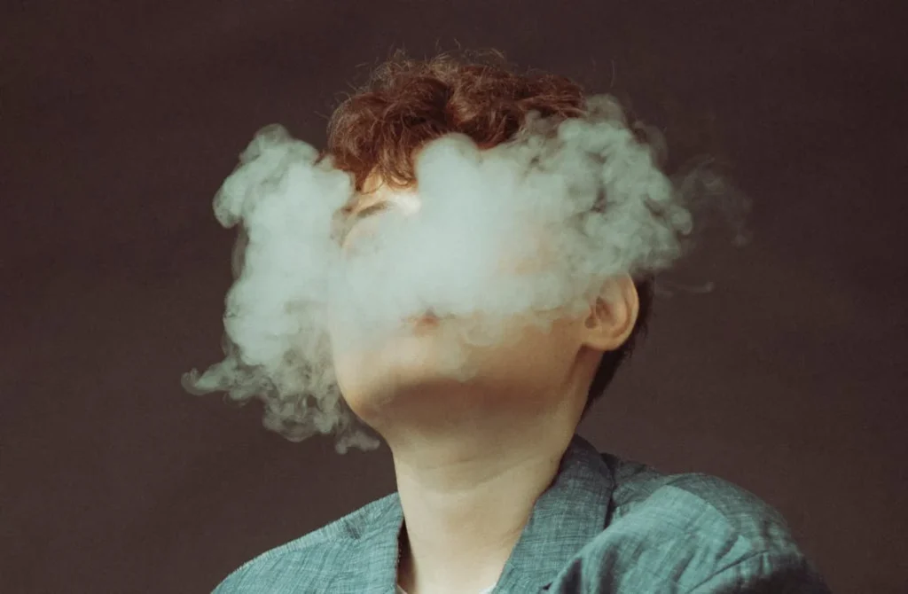 "Person exhaling a dense cloud of vapor with face obscured, symbolizing the use of a 'Terp Ready Ball Vape' device. The image highlights the effect of vaporization, showcasing a thick, cloudy exhale against a muted background."