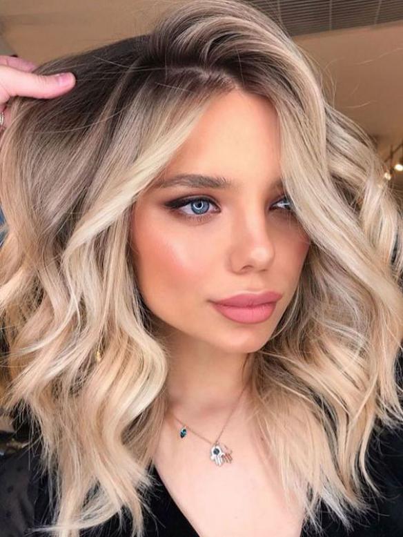 Close-up of a Glueless Human Hair Wigs with wavy blonde hair and blue eyes, wearing natural makeup and a delicate necklace. She has a confident expression and is gazing off to the side.