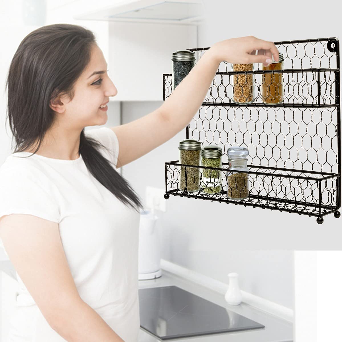 Woman organizing jars of spices on a black, wall-mounted, 2-tier wire spice rack in a kitchen setting