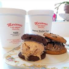 A plate with two ice cream cookie sandwiches made from chocolate and peanut butter cookies filled with ice cream. Behind them are two tubs of A plate with two ice cream cookie sandwiches made from chocolate and peanut butter cookies filled with ice cream. Behind them are two tubs of Marianne's Ice Cream labeled '1020' and 'Peanut Butter Cup,' placed on a countertop. labeled '1020' and 'Peanut Butter Cup,' placed on a countertop.