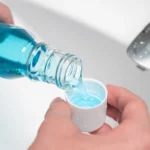 Close-up of a person pouring blue Mouthwash Burn into a cap over a bathroom sink, with a silver faucet in the background.