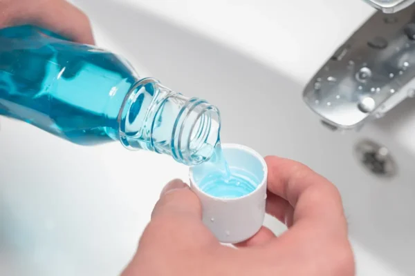 Close-up of a person pouring blue Mouthwash Burn into a cap over a bathroom sink, with a silver faucet in the background.