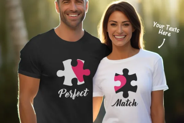 A smiling couple wearing matching puzzle piece T-shirts. The man, in a black shirt, has the word 'Perfect' printed under the puzzle piece, and the woman, in a white shirt, has the word 'Match' beneath hers. The puzzle pieces are designed to fit together, symbolizing their connection. There is an arrow pointing to the woman's shirt, labeled 'Your Texts Here,' indicating customization options.