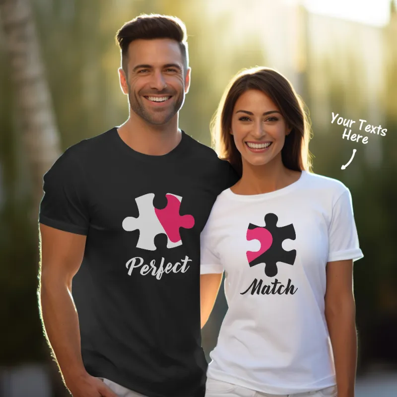 A smiling couple wearing matching puzzle piece T-shirts. The man, in a black shirt, has the word 'Perfect' printed under the puzzle piece, and the woman, in a white shirt, has the word 'Match' beneath hers. The puzzle pieces are designed to fit together, symbolizing their connection. There is an arrow pointing to the woman's shirt, labeled 'Your Texts Here,' indicating customization options.