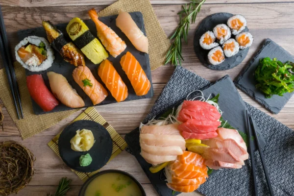 An assortment of sushi and sashimi presented on slate platters, including nigiri, maki rolls, sashimi cuts of tuna and salmon, with garnishes of wasabi, pickled ginger, and a side of seaweed salad.