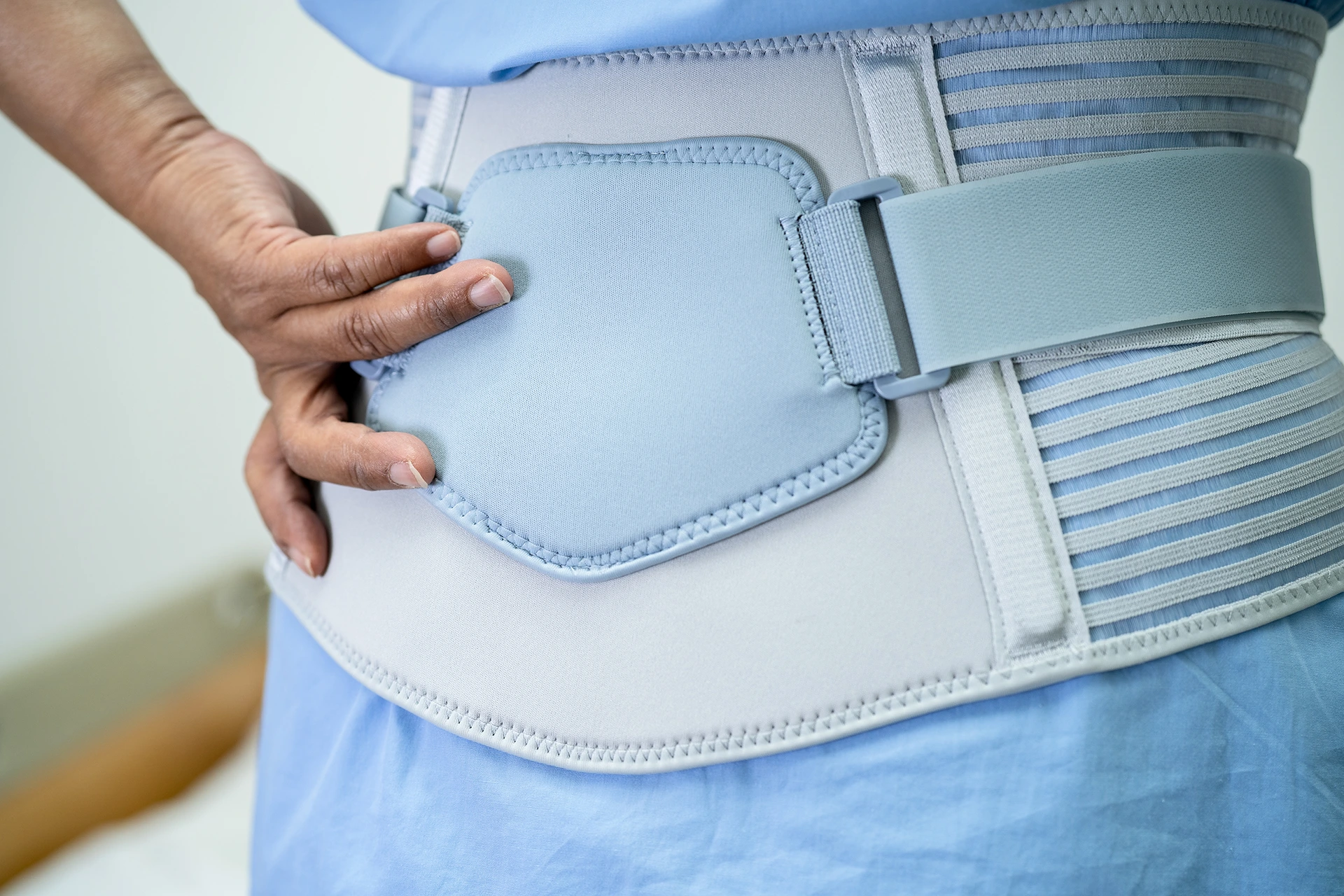 A person wearing a black adjustable Sciatica Braces wrapped around the lower back, hip, and thigh, secured with straps and highlighted by blue arrows indicating adjustable compression.