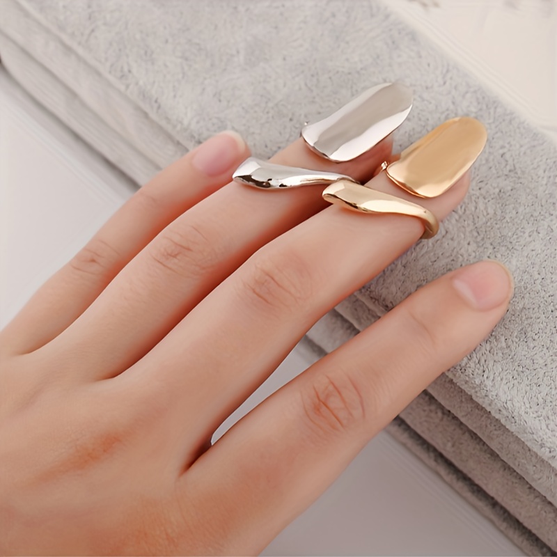 Close-up image of hands adorned with gold fingernail rings on two fingers, showcasing a unique and stylish nail accessory. The hands are neatly manicured, and one wrist is wearing a silver bangle bracelet.