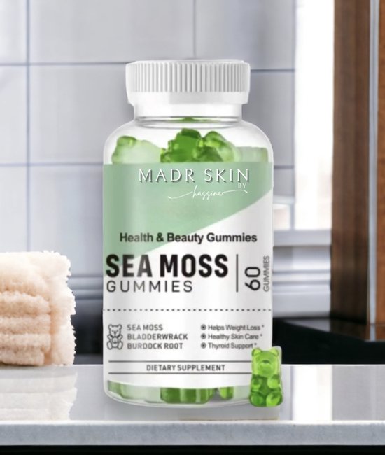 MadR Skin by Jayyana Sea Moss Gummies dietary supplement bottle placed on a bathroom counter, featuring green gummies and a label promoting health and beauty benefits such as weight loss, healthy skin care, and thyroid support, with ingredients like sea moss, bladderwrack, and burdock root. A stack of beige towels is visible beside the bottle.