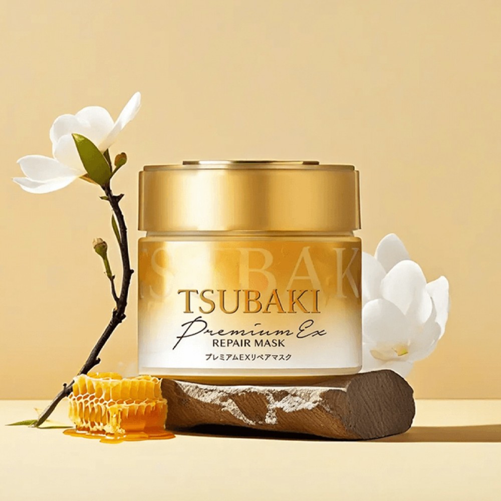 A gold jar of Tsubaki Hair Mask Premium EX Repair Mask displayed on a rustic wooden base, surrounded by white flowers and a honeycomb, set against a warm yellow background.