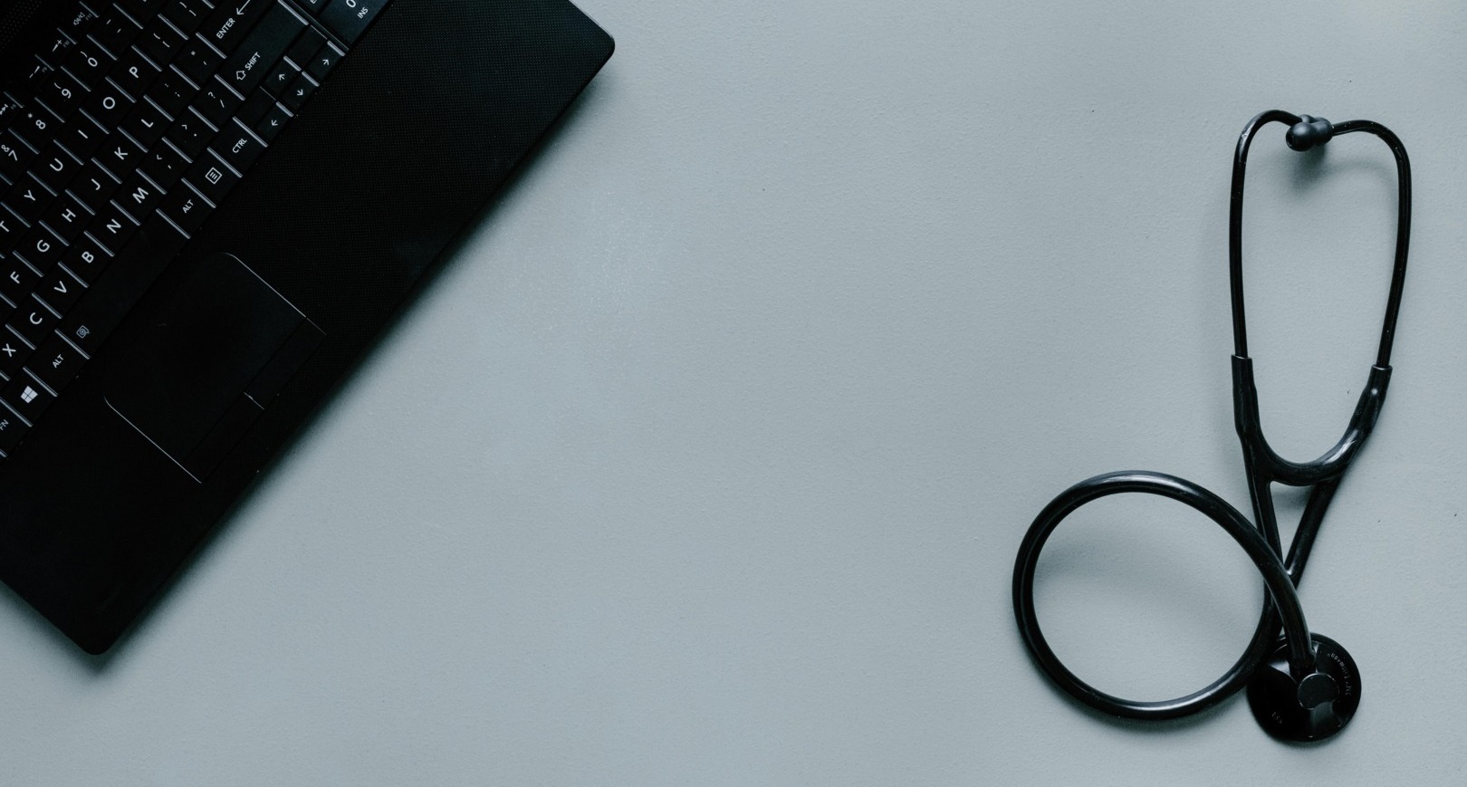 A black laptop keyboard and touchpad are partially visible on the left side of the image, while a black stethoscope is placed on the right side against a light-colored surface. Vosita